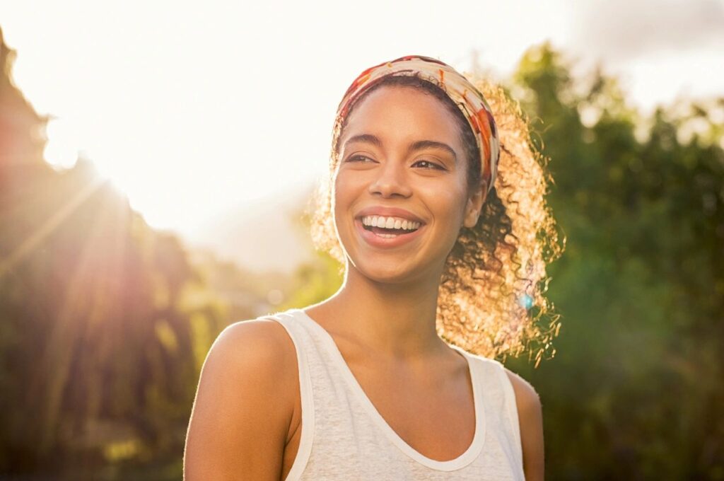 Smiling woman outdoors with sunlight background.