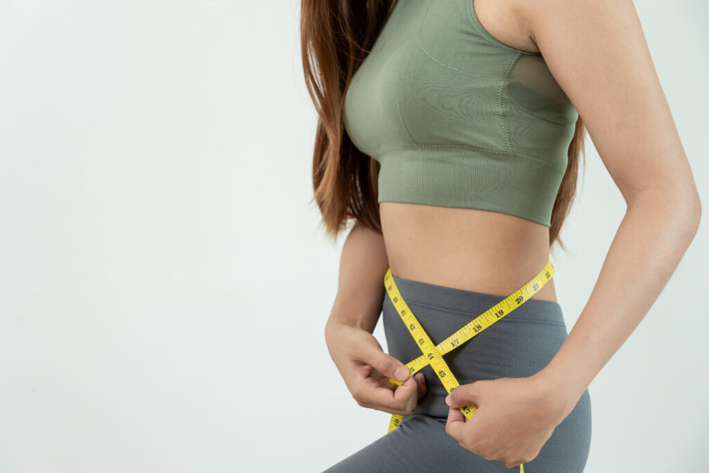 Woman measuring waist with yellow tape measure.